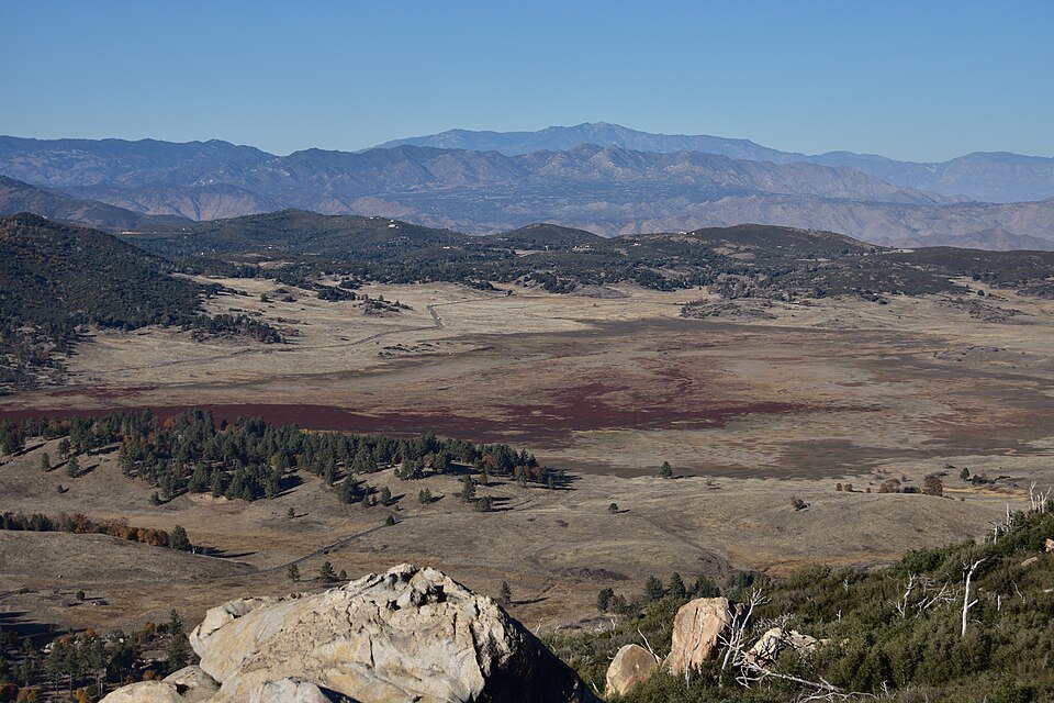 Wide mountain valley view with meadow, forest and distant ridges from a rocky summit