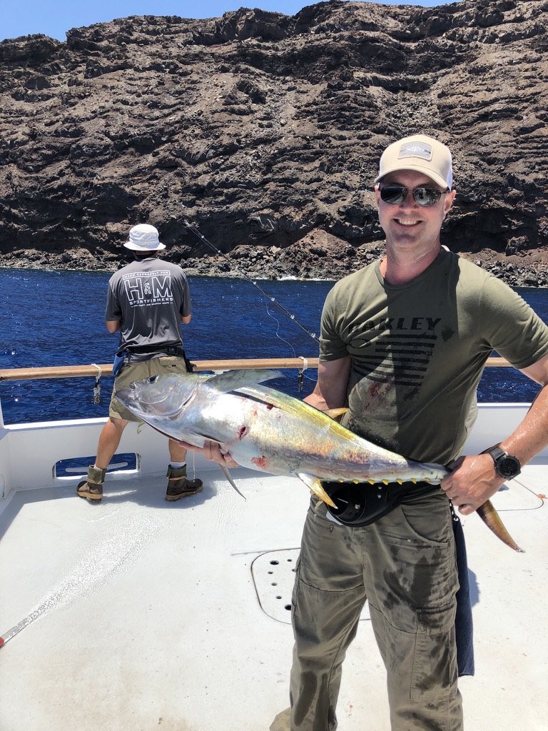 A smiling angler on deck holding a large fish, a rocky island behind
