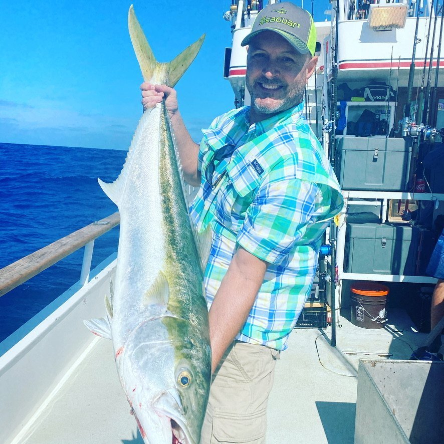 A smiling angler holding a big fish on deck in the sun