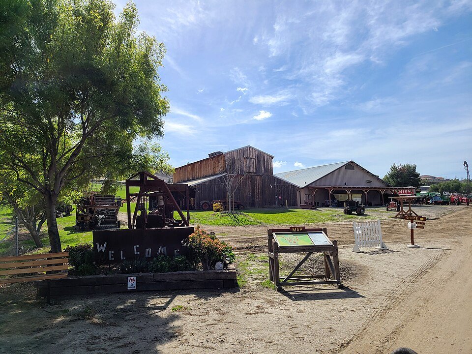 A welcome sign and old farm engines in front of wooden barns at the Antique Gas and Steam Engine Museum