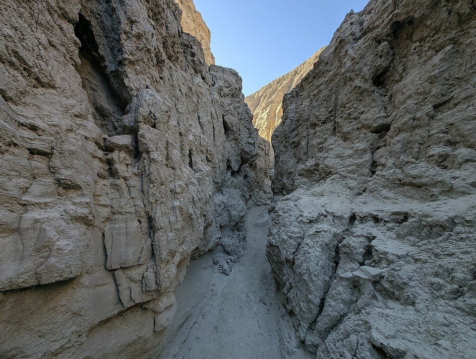 Narrow slot canyon with pale rock walls and a sandy floor