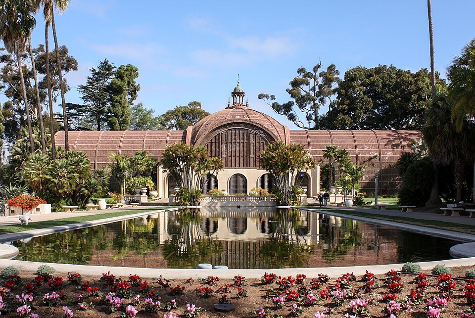 The Botanical Building and Lily Pond in Balboa Park with red flowers in front