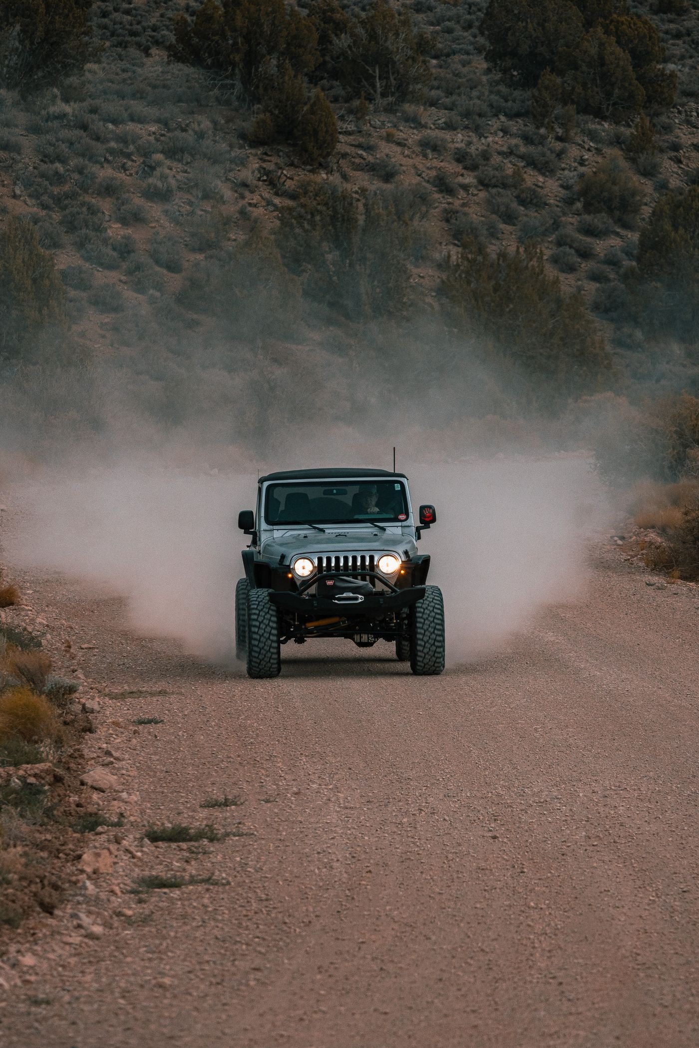 A black and gray Jeep Wrangler driving along a dirt road