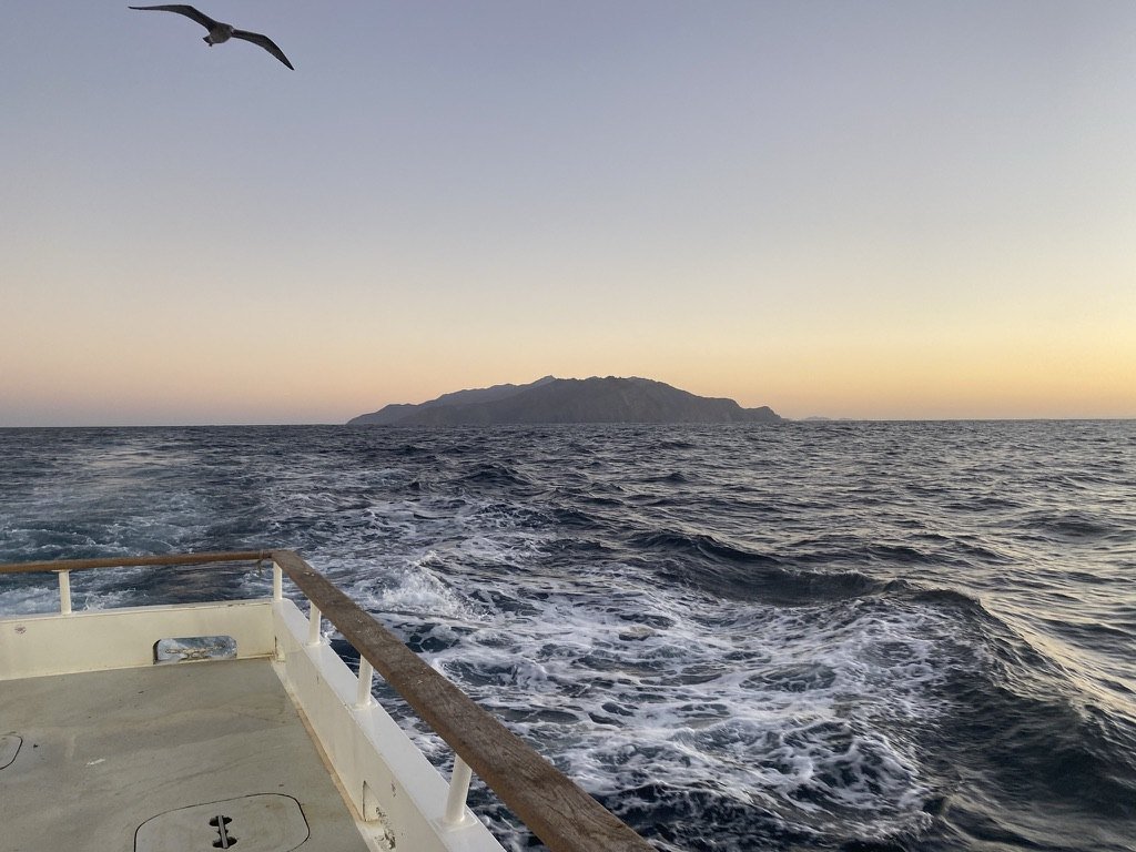 Boat wake and rail in the foreground, a low island on the horizon at dusk