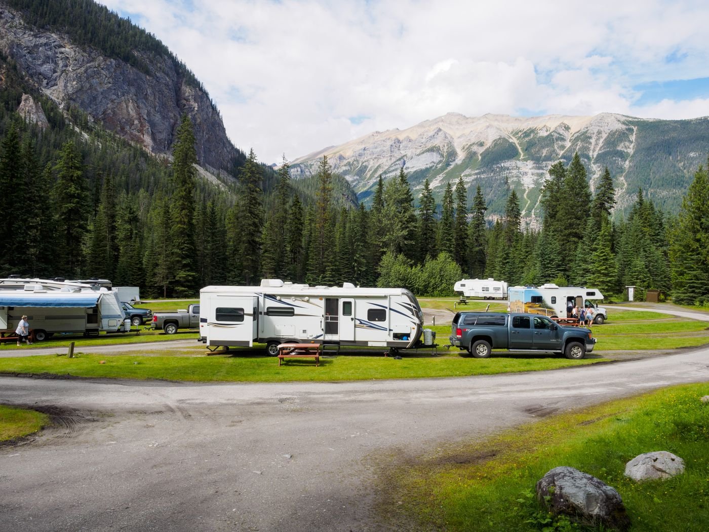 Vehicles with trailers parked at a campsite below mountains