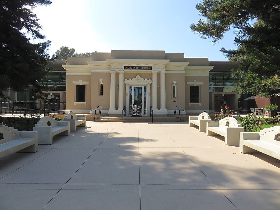 The front of the Coronado Public Library, a cream-colored building with columns, seen across a plaza