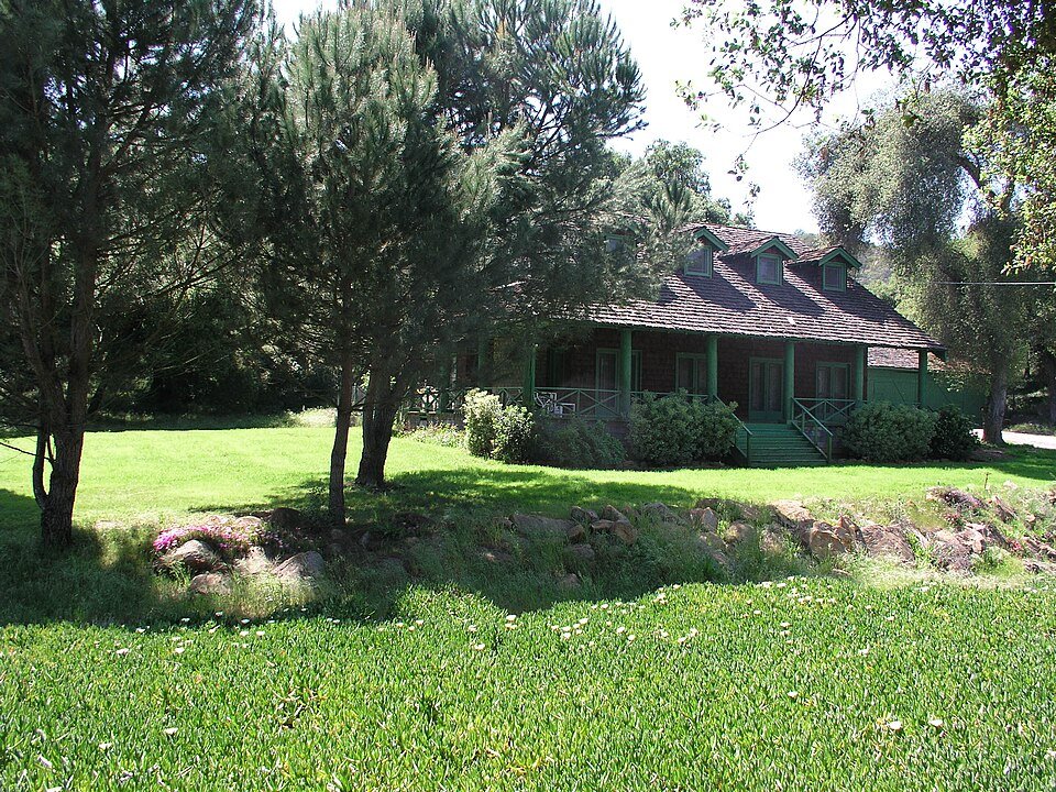 A green lodge house with a lawn and pine trees at Daley Ranch