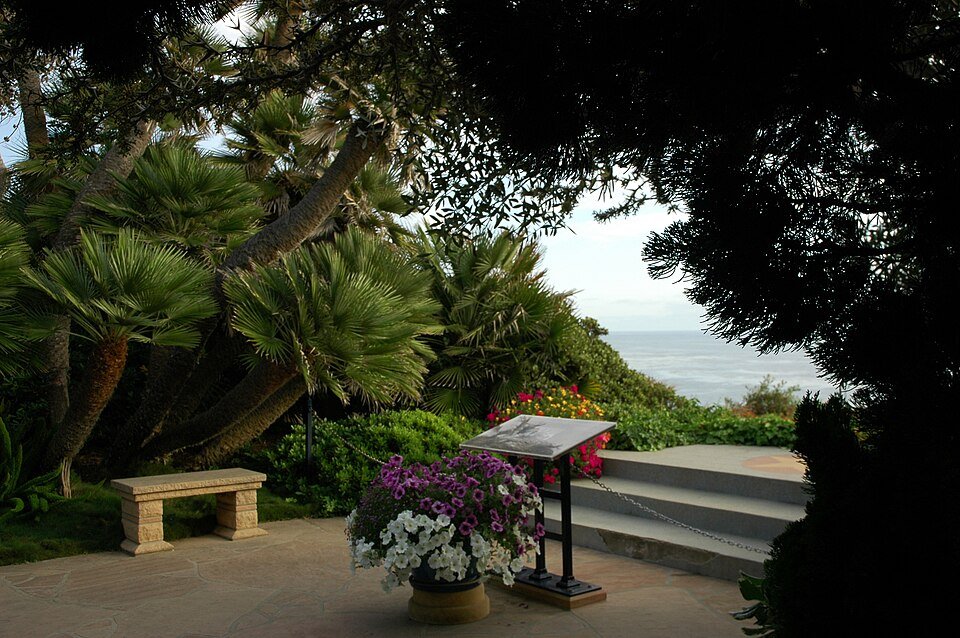 A stone bench and flowers among trees in the Meditation Gardens, looking toward the ocean