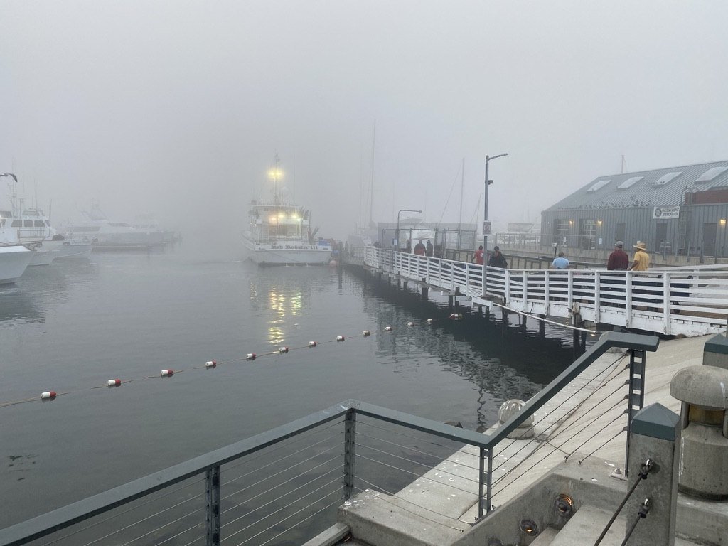 A boat with lights glowing in fog beside a railed pier