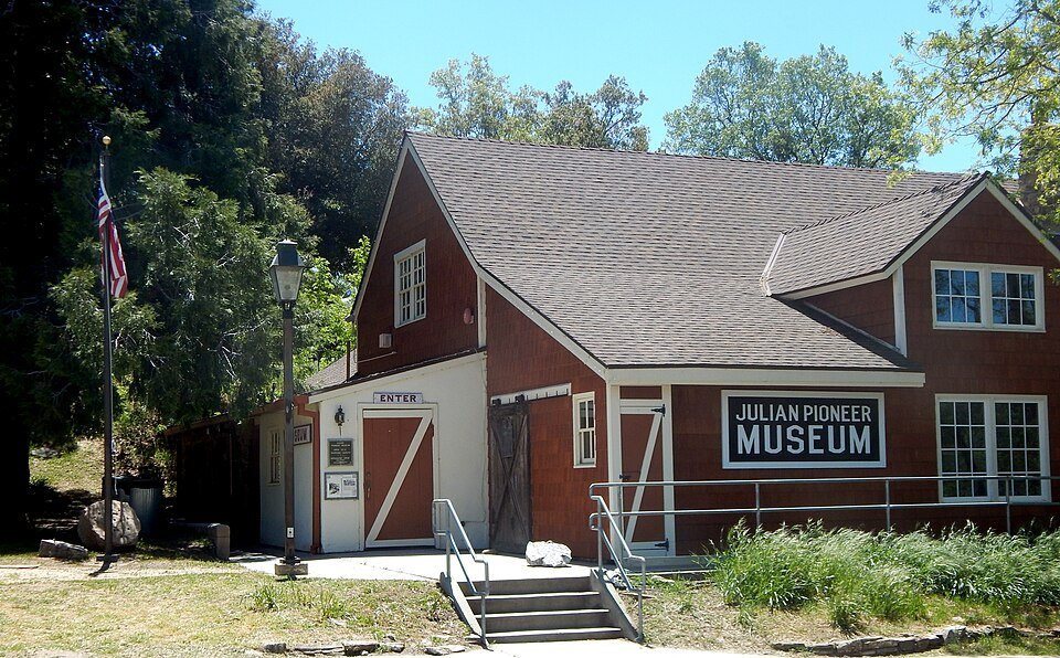 The red Julian Pioneer Museum building with a flag and trees