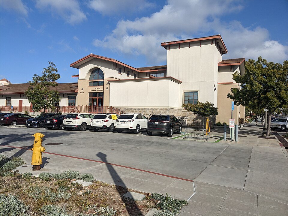 The tan stucco La Mesa Library with a tower and a parking lot