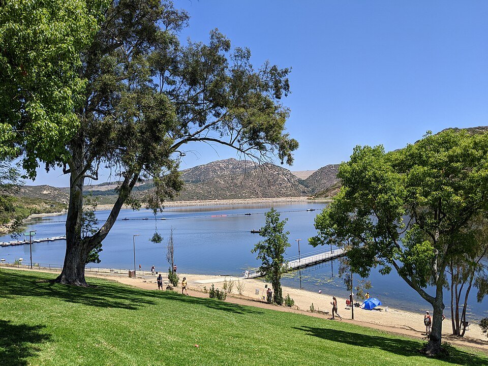 A sandy shore, floating dock and green lawn at Lake Poway with hills beyond
