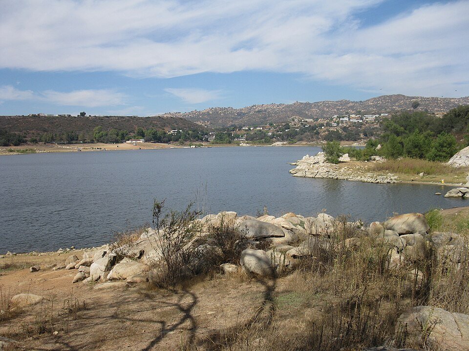 A lake with a rocky shoreline and houses on the hillside beyond.