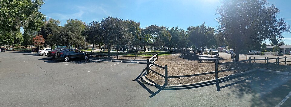 A wide view of a shaded lawn, fence and parking area at Lemon Grove Park