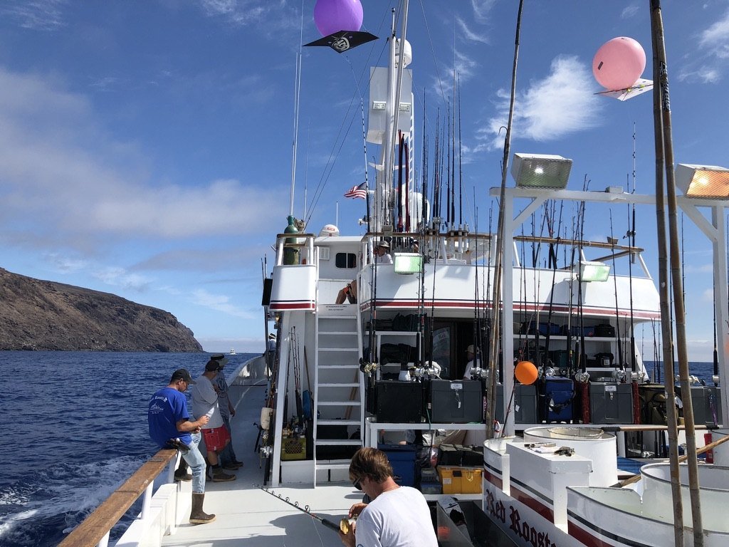 The deck of a multi-day boat with rod racks and flags, an island coastline behind