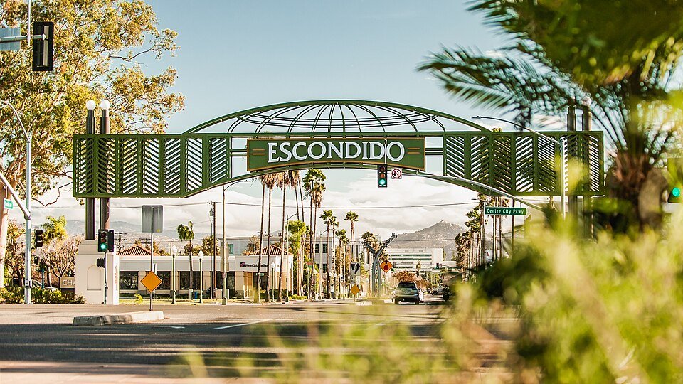 The green Escondido arch sign over Grand Avenue, with palm trees and hills behind