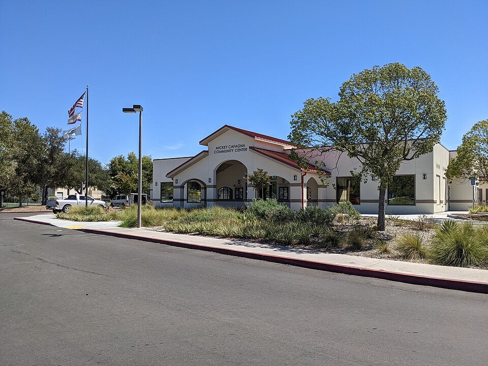 The Mickey Cafagna Community Center building with a flag and trees at Poway Community Park