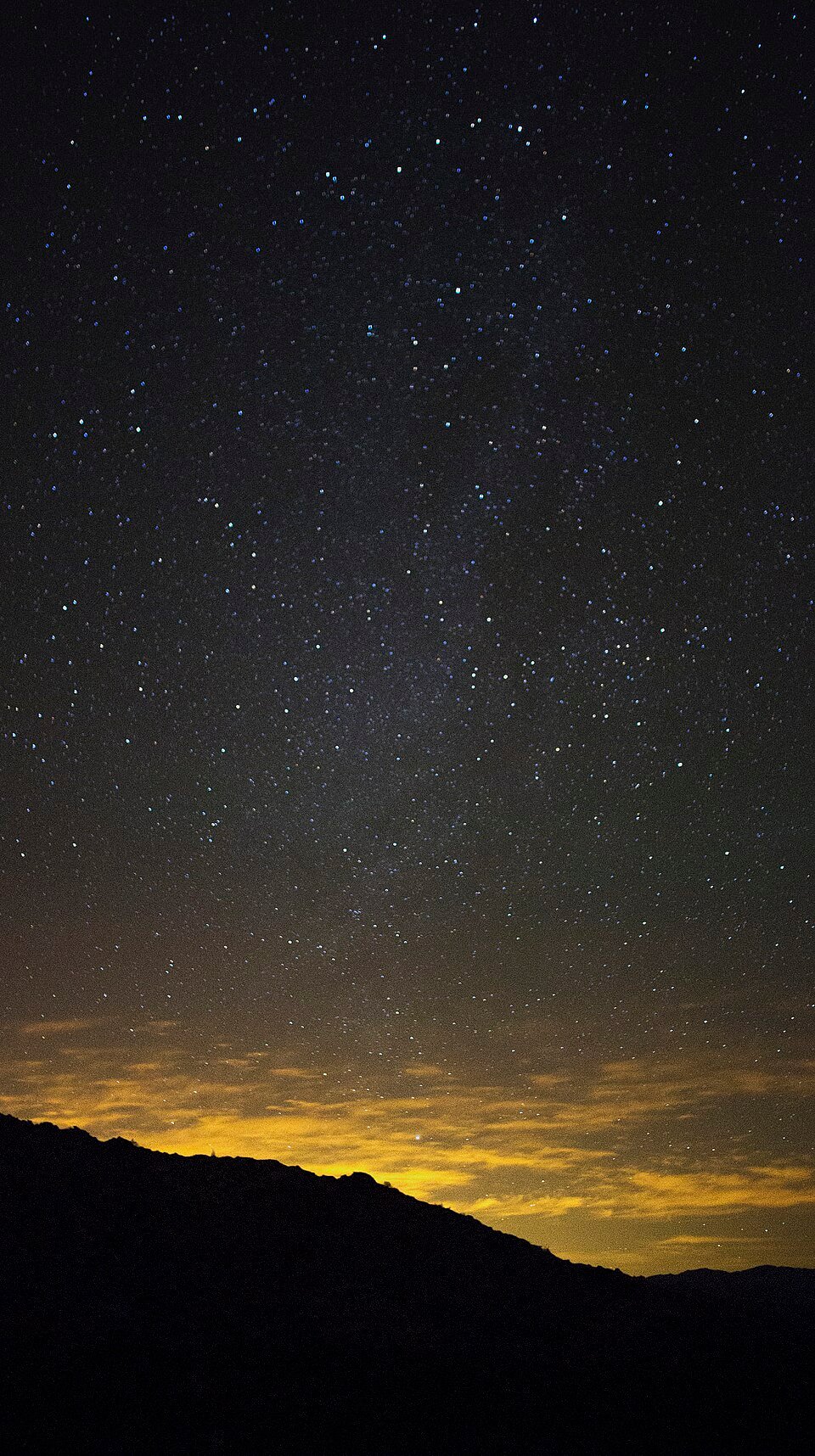 Stars over a dark desert horizon with a faint yellow glow