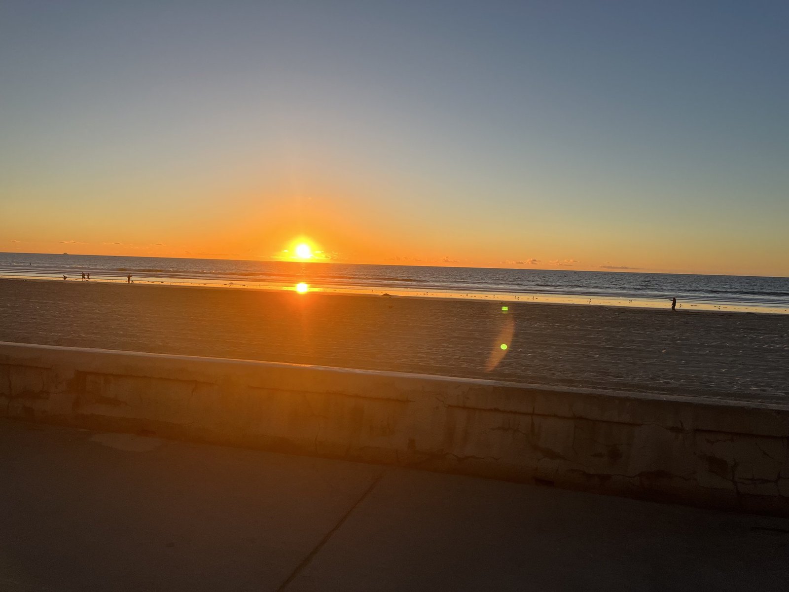 The sun setting over the ocean at Mission Beach, with sand and a concrete seawall in the foreground