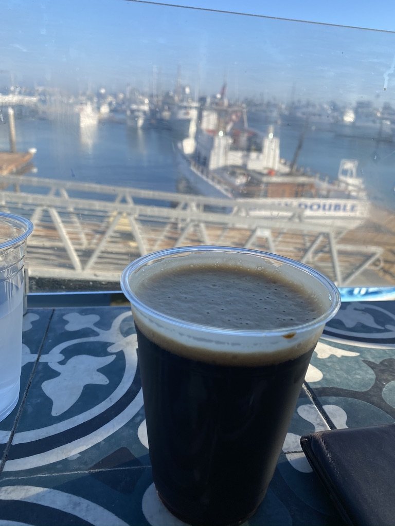 A dark stout in a clear cup on a tiled table on the patio, with a sportfishing boat at its slip beyond the glass