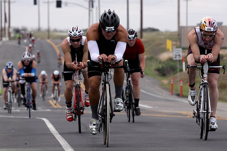 A pack of cyclists in helmets riding a road during a triathlon bike leg.