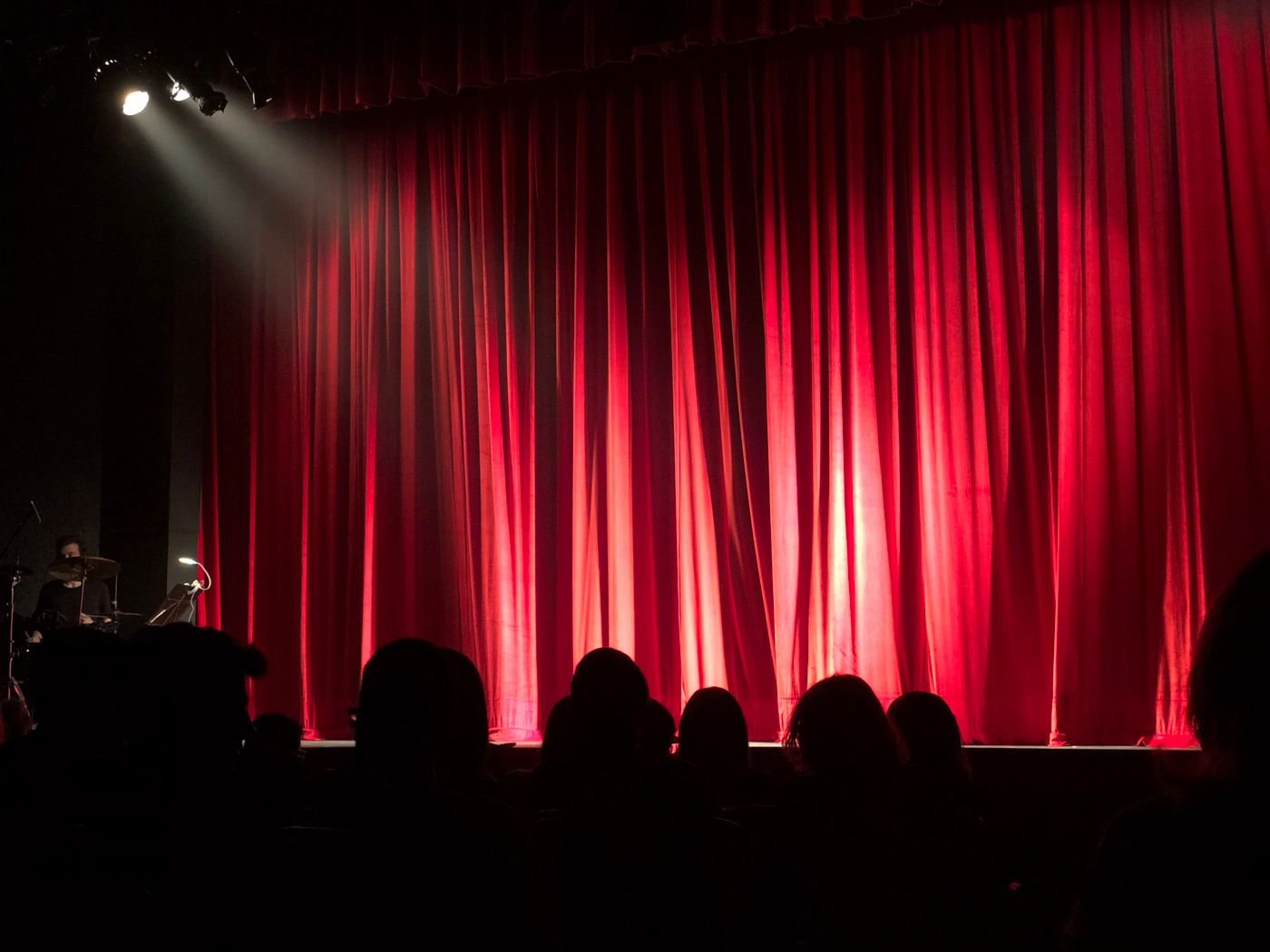 A theater audience seated before a stage with red curtains