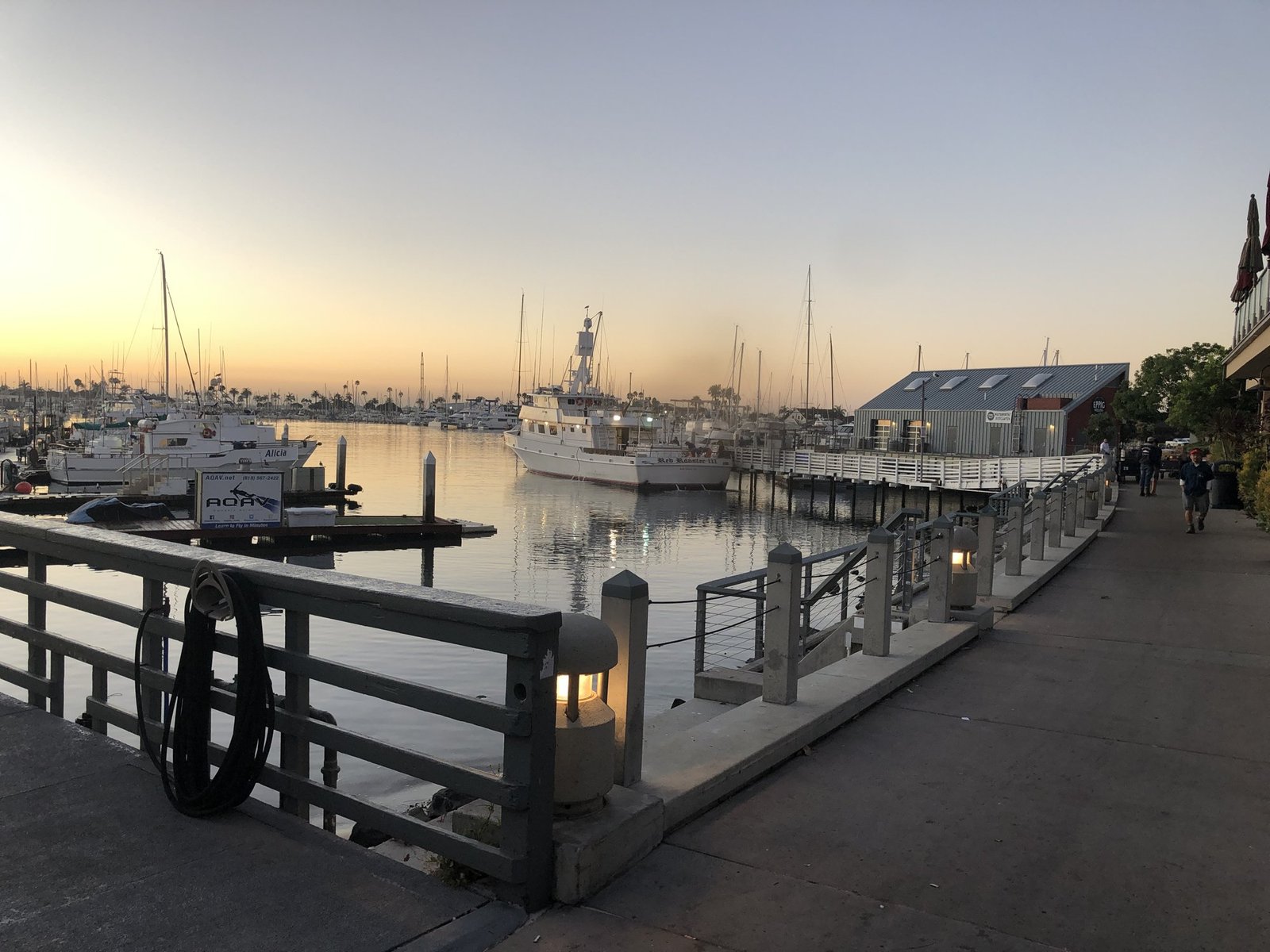 The harbor walkway at dusk in Point Loma, with boats at their slips and a pink sky