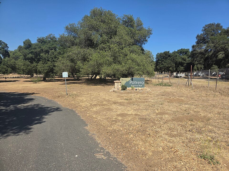 Gravel path through dry grass toward a large oak tree and a small park sign reading Potrero