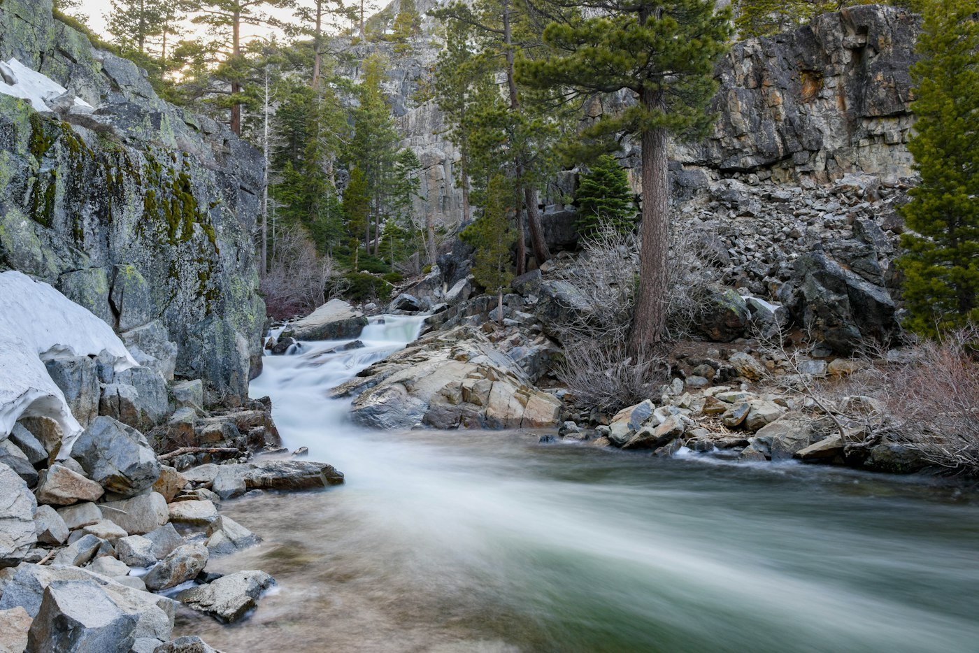 A clear river flowing between gray rocks and green banks