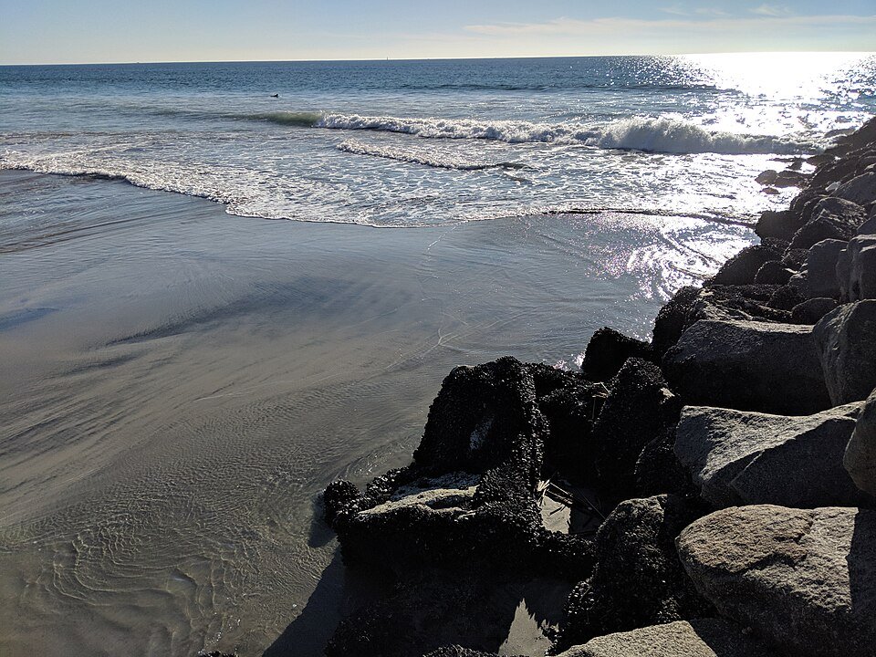 Surf washing over a rocky jetty and dark wet sand at an Oceanside beach