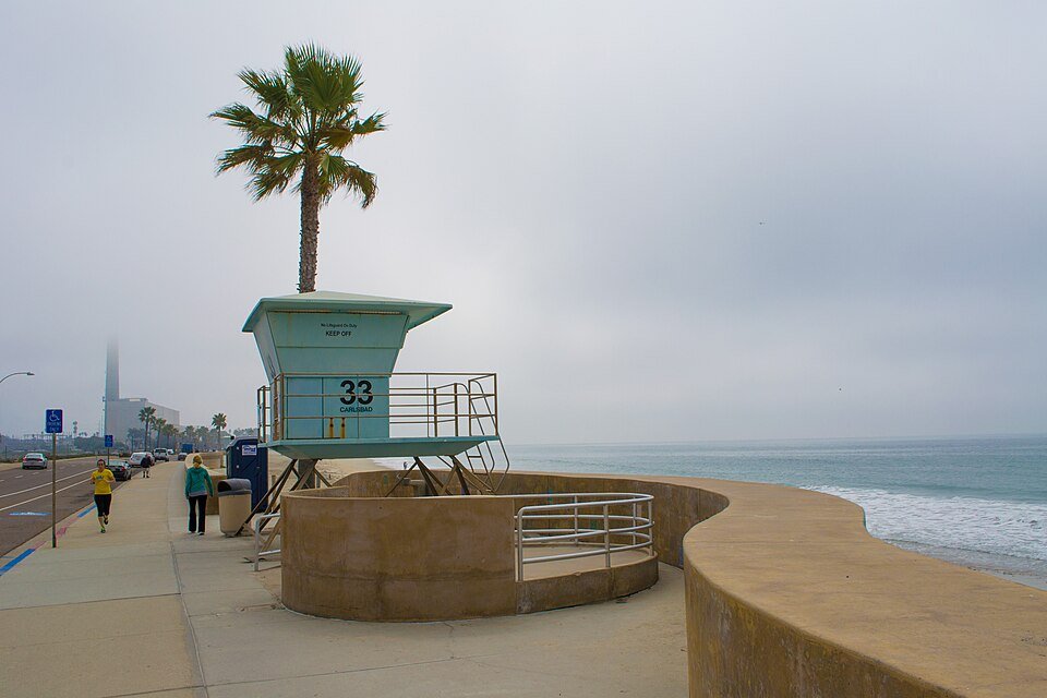 A teal lifeguard tower number 33 and a curved seawall beside the walkway on Carlsbad State Beach