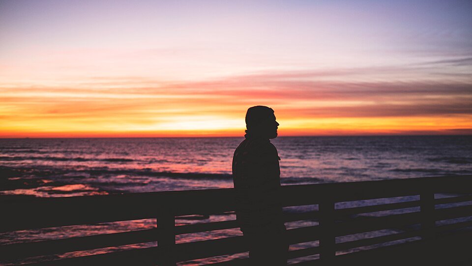 A person silhouetted against a sunset on a wooden pier railing