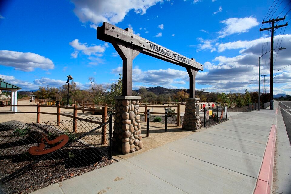 The wooden Walker Preserve entrance sign with stone posts beside a sidewalk