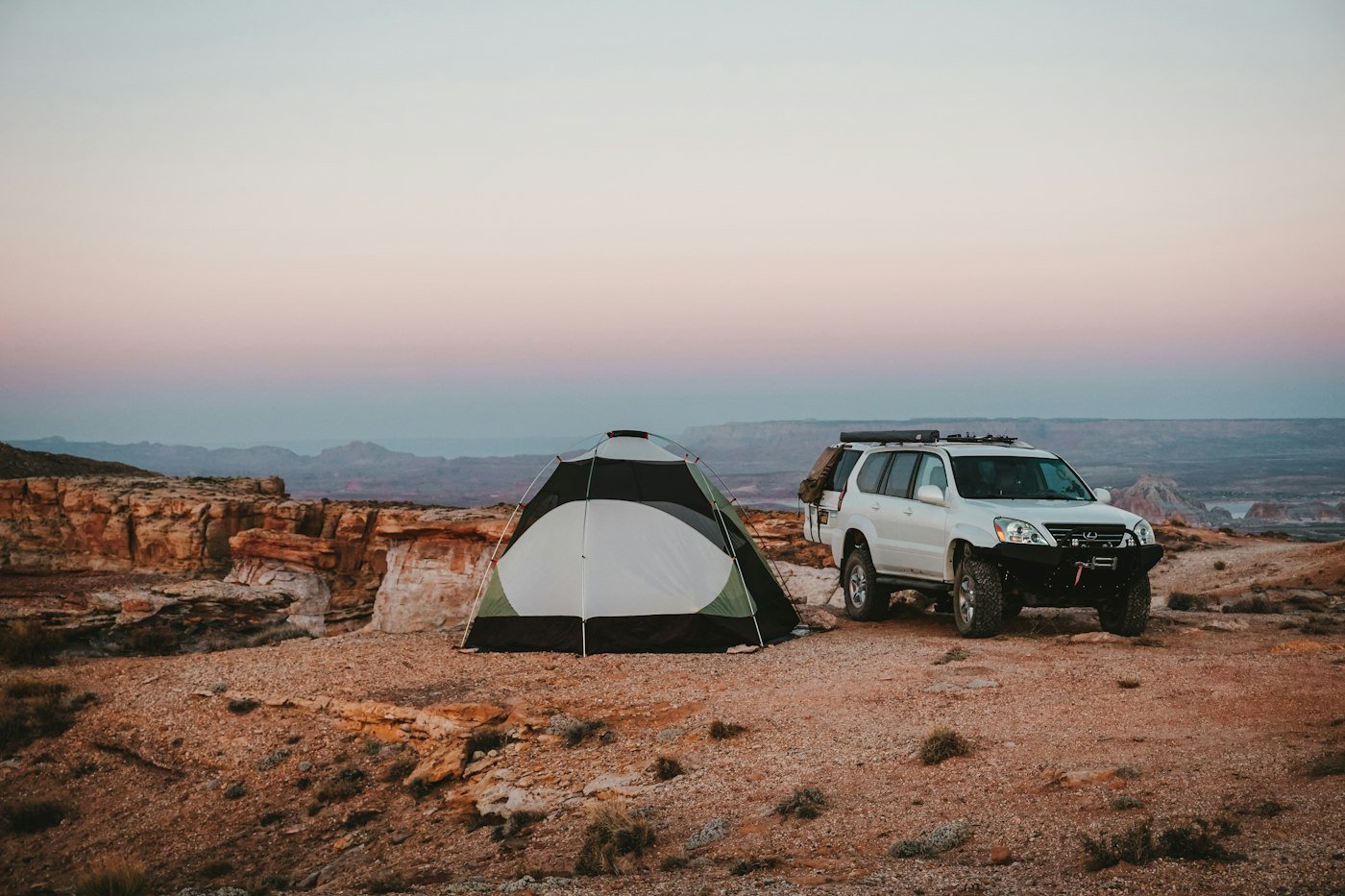 A white SUV and two tents set up on open desert ground at dusk